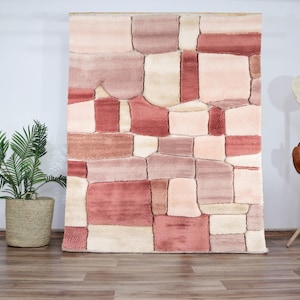 Peut inclure: Un tapis de salon rose et crème avec un motif géométrique. Le tapis est fait de fibres douces et moelleuses et présente un design moderne et abstrait.