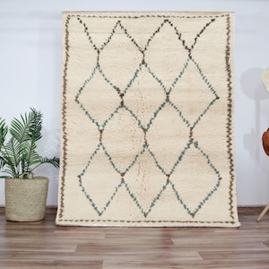 May include: A white rug with a diamond pattern in brown and blue. The rug has a fringe border.
