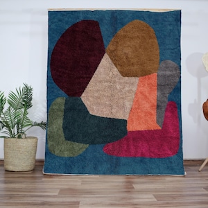 Peut inclure: Tapis abstrait avec des formes géométriques dans des tons de brun, rouge, vert, bleu et beige. Le tapis a une surface texturée et duveteuse.