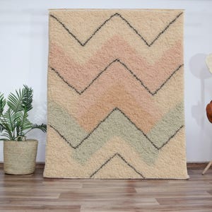 May include: A cream-colored rug with a chevron pattern in shades of pink and green. The rug has a soft, fluffy texture.