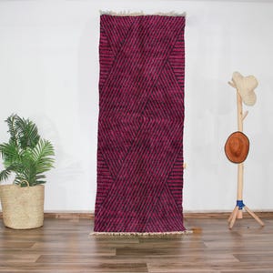May include: A long, narrow pink and black patterned rug with a geometric design. The rug is made of wool and has a fringe on both ends.