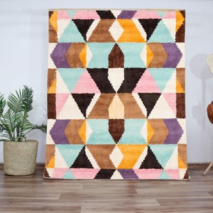 Handmade colorful wool rug featuring a bold geometric pattern with pastel pinks, blues, yellows, and earth tones. Crafted with high-quality hand-knotted wool, this modern Art Deco-inspired rug brings vibrant energy and artistic flair to living rooms, bedrooms, or creative interiors. Plush, durable, and visually striking, it creates a cozy yet dynamic atmosphere in any contemporary or eclectic space.