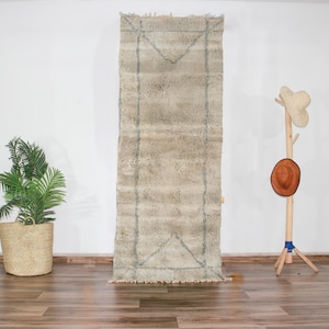 May include: A white and gray Moroccan rug with a geometric pattern. The rug is hanging on a white wall.