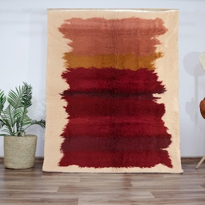 Pode incluir: Um tapete grande e abstrato com fundo branco e um design multicolorido. O design apresenta tons de rosa, laranja, vermelho e marrom. O tapete tem uma textura felpuda.