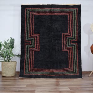 May include: A black rug with a geometric pattern in shades of green and red. The rug has a thick pile and a fringed edge.