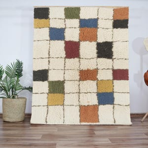 Peut inclure: Un tapis blanc à motif à carreaux de différentes couleurs, notamment rouge, bleu, vert, jaune et orange. Le tapis est fait d'un matériau doux et moelleux.