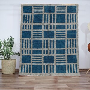 Peut inclure: Un tapis géométrique bleu et blanc avec un motif carré. Le tapis est fait d'un matériau doux et moelleux et a un léger brillant.