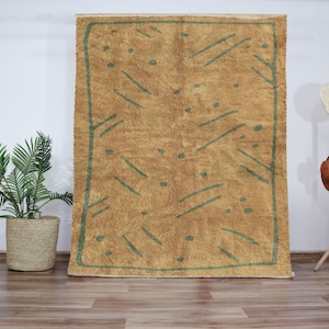 Peut inclure: Un grand tapis rectangulaire avec un fond brun et des motifs géométriques verts. Le tapis a une bordure frangée.