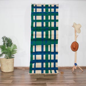 Peut inclure: Un tapis rectangulaire à motifs géométriques blancs et bleus avec des accents verts. Le tapis est suspendu à un mur blanc.