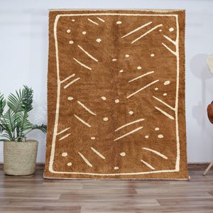 以下が含まれることがあります： 茶色と白の幾何学模様の敷物。敷物は白い縁取りがあり、柔らかくふわふわした素材でできています。