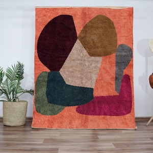 Op de afbeelding: Abstract tapijt met een geometrisch ontwerp in tinten bruin, groen, roze en beige op een oranje achtergrond.