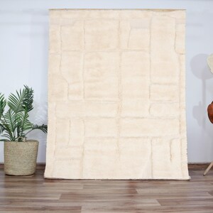 Peut inclure: Un tapis en fourrure blanche avec un motif géométrique. Le tapis a une texture en relief et est fait de fibres douces et moelleuses.