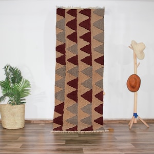 Può includere: Un tappeto marrone e beige con un motivo geometrico di triangoli. Il tappeto ha un bordo a frangia.