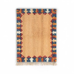 Authentic Moroccan Beni Ourain wool rug with warm ochre field and bold multicolor geometric border, handmade using 100% wool by Berber artisans; features rich earth tones of terracotta, blue, ivory, and rust; perfect for modern boho homes, Japandi, or rustic decor styles; this luxurious Moroccan wool carpet adds warmth and tribal charm to living rooms, dining rooms, or entryways while celebrating timeless craftsmanship from the Atlas Mountains.