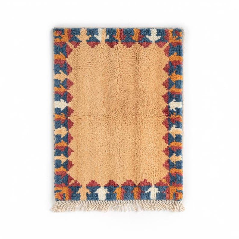 Authentic Moroccan Beni Ourain wool rug with warm ochre field and bold multicolor geometric border, handmade using 100% wool by Berber artisans; features rich earth tones of terracotta, blue, ivory, and rust; perfect for modern boho homes, Japandi, or rustic decor styles; this luxurious Moroccan wool carpet adds warmth and tribal charm to living rooms, dining rooms, or entryways while celebrating timeless craftsmanship from the Atlas Mountains.