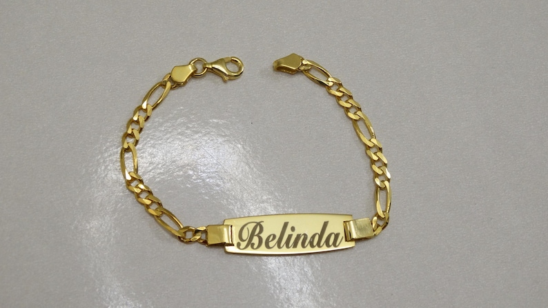 Puede incluir: Un brazalete de cadena dorada con una placa rectangular con el nombre "Belinda".