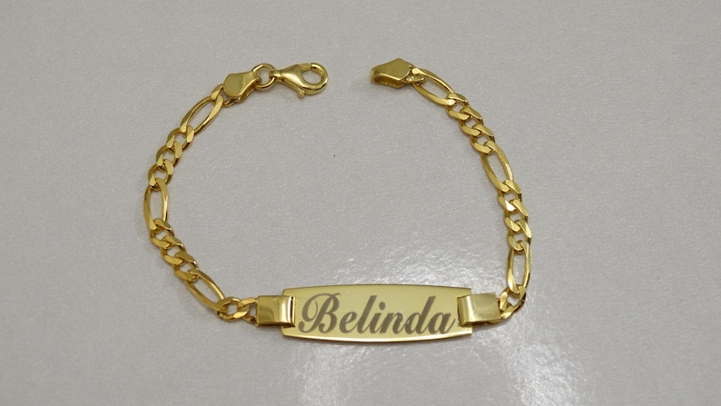 Puede incluir: Un brazalete de cadena de oro con una placa rectangular grabada con el nombre "Belinda".