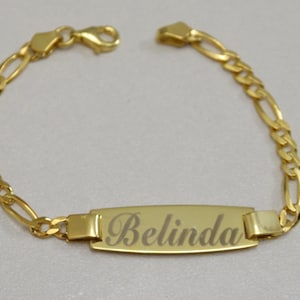 Puede incluir: Un brazalete de cadena dorada con una placa rectangular grabada con el nombre "Belinda".