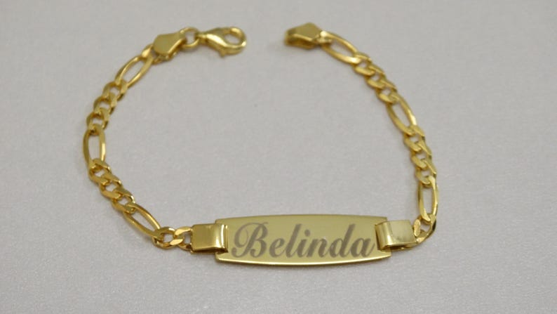 Puede incluir: Un brazalete de cadena dorada con una placa rectangular grabada con el nombre "Belinda".