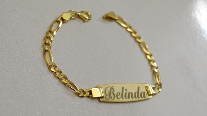 Puede incluir: Pulsera de cadena dorada con una placa rectangular grabada con el nombre "Belinda".