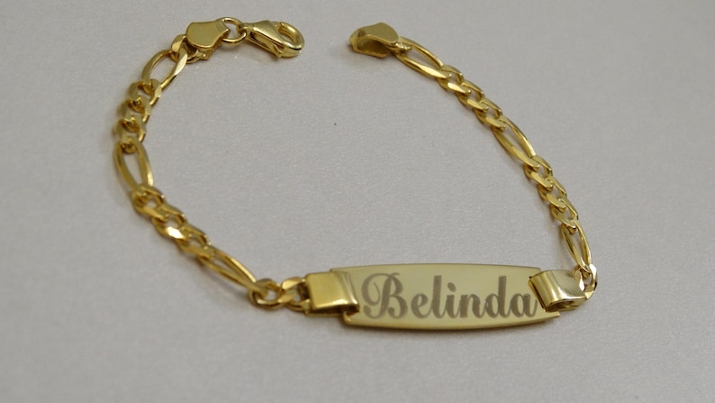 Puede incluir: Un brazalete de cadena de oro con una placa rectangular grabada con el nombre "Belinda".