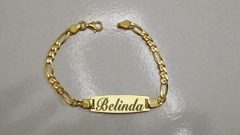 Puede incluir: Pulsera de cadena dorada con una placa rectangular con el nombre "Belinda".