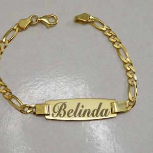 Puede incluir: Un brazalete de cadena dorada con una placa rectangular que dice "Belinda".
