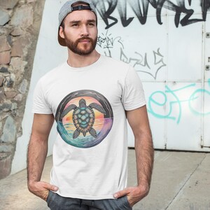 May include: White t-shirt featuring a circular graphic of a sea turtle with a sunset background. The turtle is detailed with blue, green, and black, set against a backdrop of orange, pink, and purple hues. The shirt is a casual wear item.