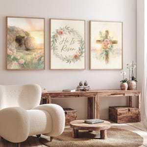 Pode incluir: Três impressões de arte em aquarela emolduradas. A primeira retrata um túmulo vazio com um nascer do sol. A segunda apresenta uma coroa floral com o texto "He Is Risen". A terceira mostra uma cruz adornada com flores.