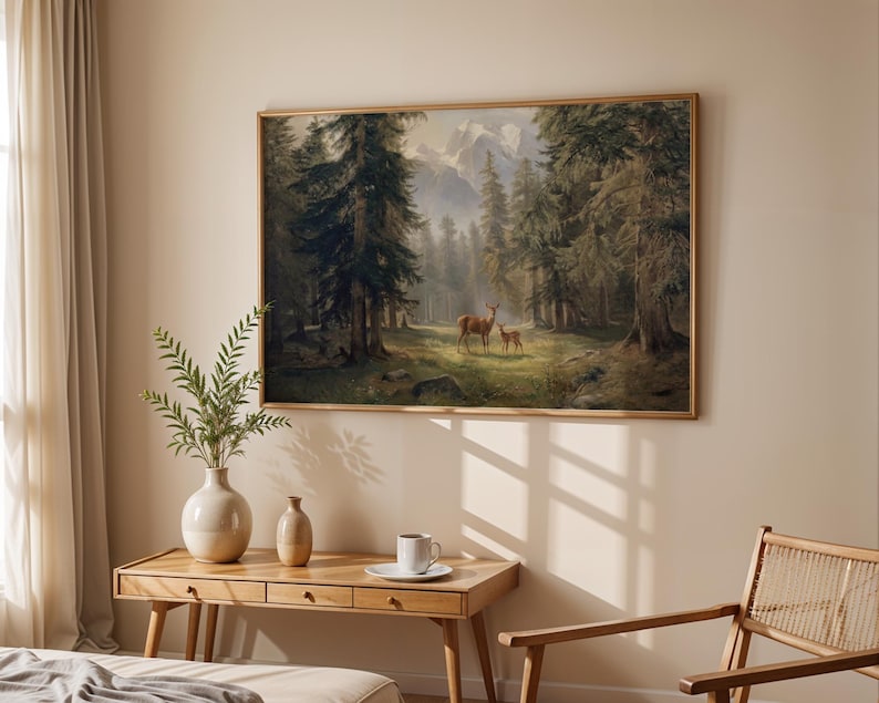 May include: A framed landscape painting depicts a forest scene with tall evergreen trees, mountains, and two deer. The artwork is displayed above a wooden desk with a vase, a small decorative vase, and a cup and saucer.