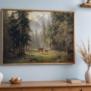May include: A framed landscape painting depicts a forest scene with tall evergreen trees and a pair of deer in a clearing. The artwork has a warm color palette and is displayed on a wooden cabinet.