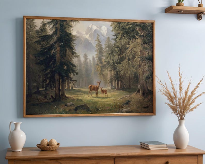 May include: A framed landscape painting depicts a forest scene with tall evergreen trees and a pair of deer in a clearing. The artwork has a warm color palette and is displayed on a wooden cabinet.