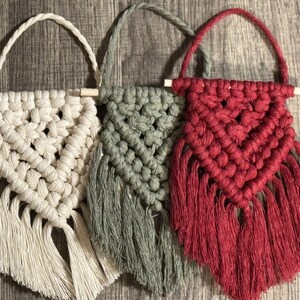 May include: Three macrame wall hangings with fringe. The hangings are made with natural fibers and are in the colors white, green, and red.