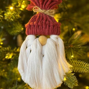 May include: A red and white crocheted gnome ornament with a wooden nose. The gnome is wearing a red hat with a white pom-pom and a white beard.