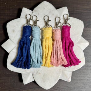 May include: Five colorful tassel keychains with silver key rings. The tassels are navy blue, light blue, yellow, pink, and magenta.