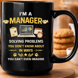 May include: Black ceramic coffee mug with the text "I'M A MANAGER" in yellow. The mug features graphics of a laptop, calendar, and alarm clock. The text below reads "SOLVING PROBLEMS YOU DON'T KNOW ABOUT IN WAYS YOU CAN'T EVEN IMAGINE."