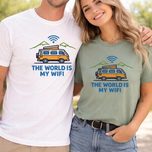 May include: White and sage green t-shirts with a graphic of a yellow camper van, mountains, and a WiFi symbol. The text on the shirts reads "THE WORLD IS MY WIFI". The shirts are worn by two people.