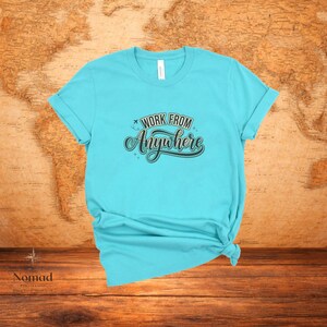 Pu&ograve; includere: Una maglietta turchese con le maniche arrotolate. La maglietta presenta la scritta "Work From Anywhere" in un carattere decorativo. La maglietta &egrave; annodata in basso. Lo sfondo &egrave; una mappa del mondo.