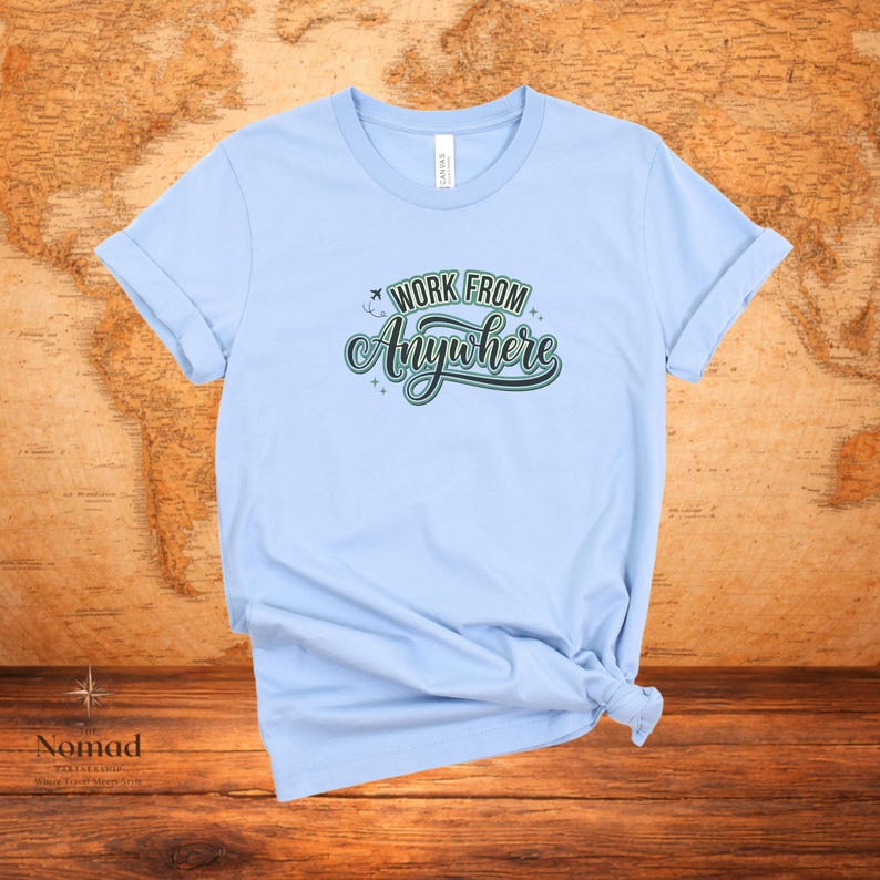 Pu&ograve; includere: T-shirt azzurra con maniche arrotolate. La maglietta presenta la scritta "WORK FROM Anywhere" in un design verde e bianco. La maglietta &egrave; annodata in basso. Lo sfondo &egrave; una mappa del mondo.