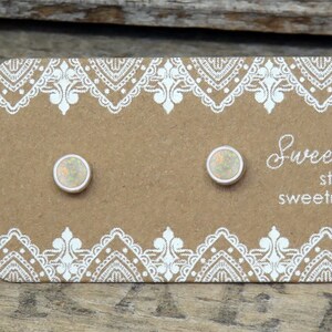 May include: Two round stud earrings with iridescent stones set in silver, displayed on a rectangular brown card with white lace-patterned borders. The card features the text Sweet Rock Candy, sterling silver .925, and sweetrockcandy.etsy.com.