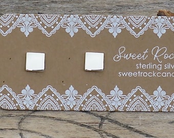 May include: A pair of small, square, polished silver stud earrings attached to a rectangular brown display card. The card features a white lace-like border pattern and the printed text Sweet Rock Candy, sterling silver .925, and sweetrockcandy.etsy.com.