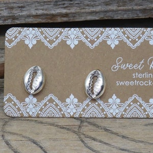 May include: A pair of sterling silver cowrie shell stud earrings attached to a rectangular brown display card with white lace-style borders. The card features the text Sweet Rock Candy, sterling silver .925, and sweetrockcandy.etsy.com in white.