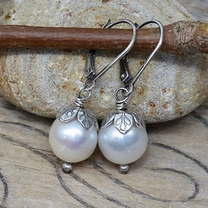 May include: A pair of silver dangle earrings with white pearl drops and leaf-shaped accents.