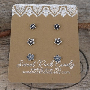 May include: A set of six sterling silver earrings on a brown card. The earrings are in the shape of a rose and a flower. The card has the text "Sweet Rock Candy" and "sterling silver .925" on it.