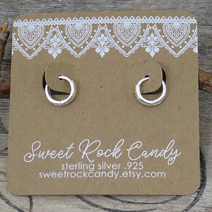 May include: A pair of small silver hoop earrings attached to a brown cardboard display card. The card features a white lace-style border at the top and the text Sweet Rock Candy, sterling silver .925, and sweetrockcandy.etsy.com printed in white.