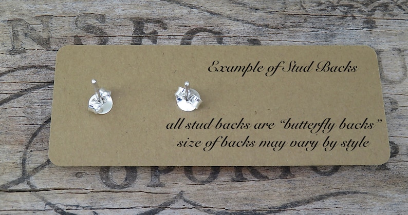 May include: A close-up of two silver earring backs on a tan card. The card has text that reads "Example of Stud Backs" and "all stud backs are 'butterfly backs' size of backs may vary by style."