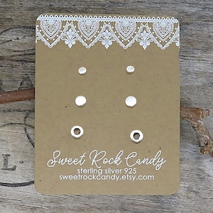 May include: A set of three pairs of silver stud earrings displayed on a rectangular brown card with white lace-style trim. The card features the text Sweet Rock Candy, sterling silver 925, and the website address sweetrockcandy.etsy.com.