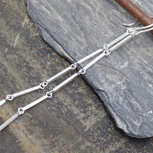 May include: Silver dangle earrings with a minimalist design featuring multiple thin, straight bars connected by small rings.