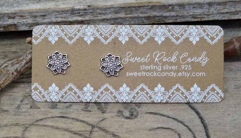 May include: A pair of sterling silver .925 flower stud earrings on a brown card with white lace trim. The card reads "Sweet Rock Candy" and the website address. The earrings are small, detailed, and have a floral design.
