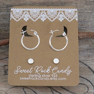May include: A pair of silver hoop earrings and a pair of silver stud earrings displayed on a brown cardboard card. The card features a white lace pattern at the top and the text Sweet Rock Candy, sterling silver 925, and sweetrockcandy.etsy.com.